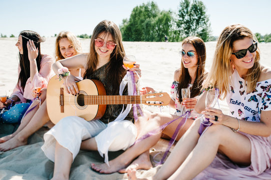 Beautiful happy slim stylish sexy young girls sitting sand beach drink champagne Play guitar. hand decorated with ribbons flowers. Party. Style boho. Maiden evening Hen-parties. Bachelorette. Close up