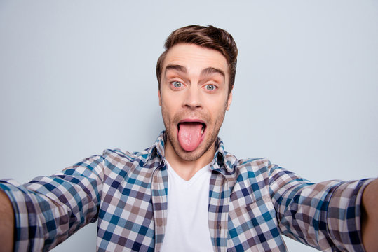 Self portrait of bearded, cheerful, stylish, cool guy in casual outfit, checkered shirt showing tongue-out to the camera over grey background