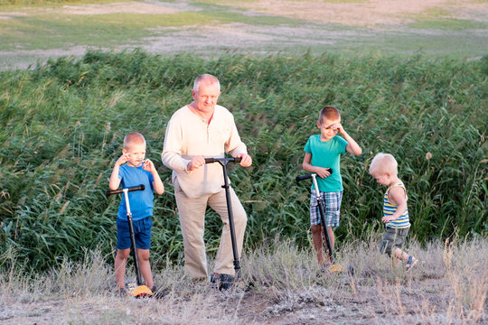 Happy children with their father on a walk in the village. Boys learn to ride a scooter on a sunny summer day. Children play outdoors with scooters. Active leisure and outdoor sports for children.