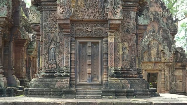 wide panning shot of two carved stone devata at banteay srei temple, cambodia
