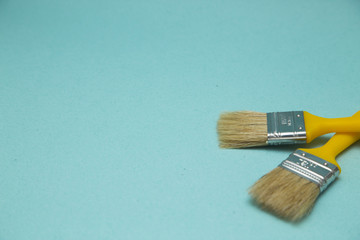 Painting the house. Two yellow paint brushes on blue background with copy space, top view, flat lay