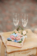 Wooden box with pink and sky blue flowers on the table, two glasses on background