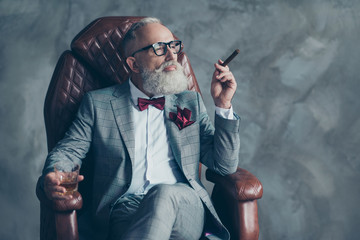 Portrait of posh chic classy virile dreamy trendy dreaming groomed brutal big company chief millionaire sitting on leather armchair smoking cigarette drinking beverage isolated on grey background © deagreez