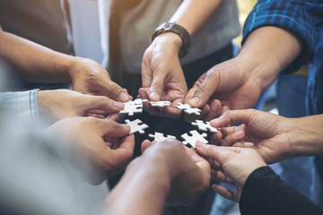 Closeup image of many people hands holding a jigsaw puzzle in circle together
