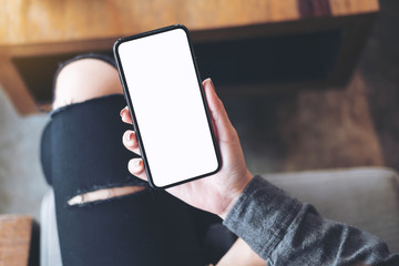 Top view mockup image of a woman holding white mobile phone with blank black desktop screen on thigh in cafe