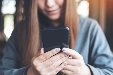 Closeup image of a beautiful Asian woman holding , using and looking at smart phone in modern cafe
