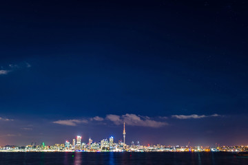 Fototapeta premium Clear starry sky above Auckland city’s skyline with the harbour, the ocean and some boats at the front