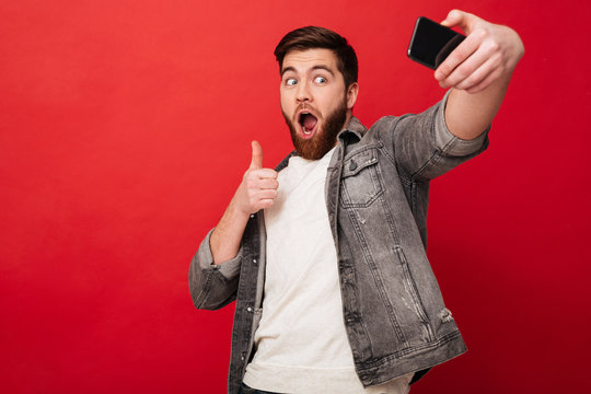 Joyful man making selfie on smartphone and showing thumb up