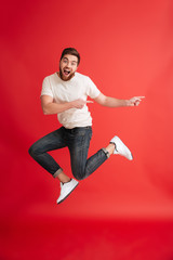Emotional bearded man jumping pointing to copyspace.