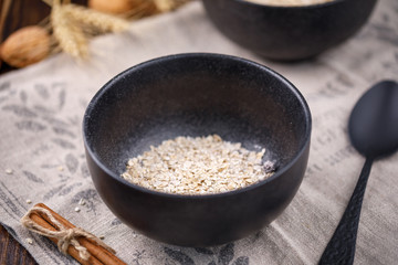 Dry flakes of oatmeal in a black bowl. Still-life on a wooden background.