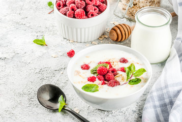 Raw ingredients for summer healthy breakfast, cereals (oats), fresh Raspberry, mint leaves, yoghurt, honey, on light concrete background, copy space