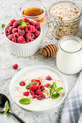 Raw ingredients for summer healthy breakfast, cereals (oats), fresh Raspberry, mint leaves, yoghurt, honey, on light concrete background, copy space