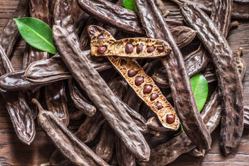 Carob pods and carob beans on the wooden table.