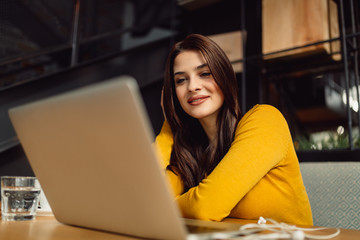 Happy brunette using laptop in cafe.