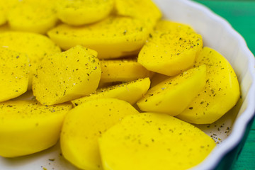 Sliced raw potatoes with spices on a dish for baking.