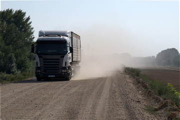 Heavy truck on gravel road dust cloud behind
