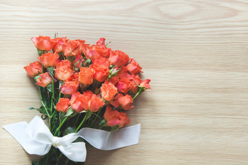 Spring concept. Bouquet of orange roses with white ribbon on wooden board. Top view. Romantic or Valentine's card.