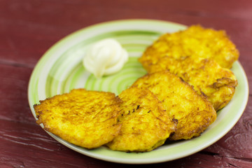 Potato pancakes on a light pink plate on a dark red wooden background.