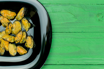 Mussels on a black plate on a wooden green background.