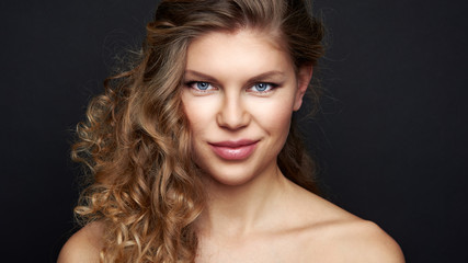 Fototapeta premium Beautiful female with curly hairstyle posing in studio. Portrait of pretty young model with waved hair over black background. 