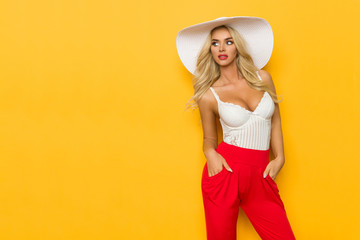 Sexy Blond Woman In White Sun Hat, Corset And Red Trousers Is Looking Away