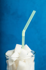 Glass with lump sugar isolated on blue background, vertical close up.
