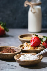 Ingredients for cooking chocolate mug cakes. Flour, cocoa powder, sugar, caramel in wooden bowls, milk, strawberries and mint served with spoons and mug over grey kitchen table. Close up