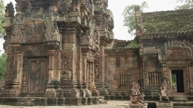 wide panning shot of two carved stone devata at banteay srei temple, cambodia