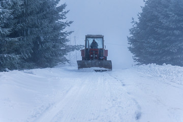 Red snowblower grader clears snow covered ski resort road.