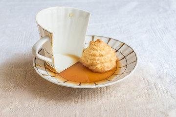 broken porcelain cup with tea and cookie on cotton tablecloth