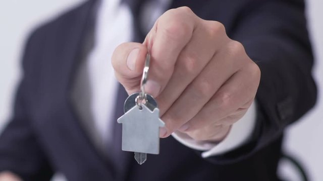 Hands of male realtor giving keys from cottage to his client, lease, close up