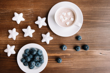 Delicious and healthy fresh blueberries with a cup of hot chocolate topped with marshmallow on the wooden table background, winter flower bouquet in a vase