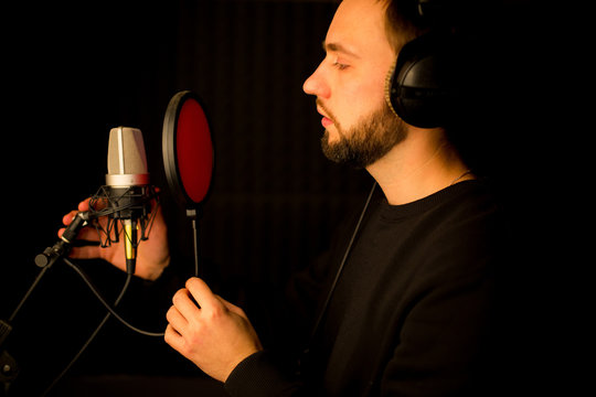Male vocalist singing into microphone in recording studio. Creating new hit song.