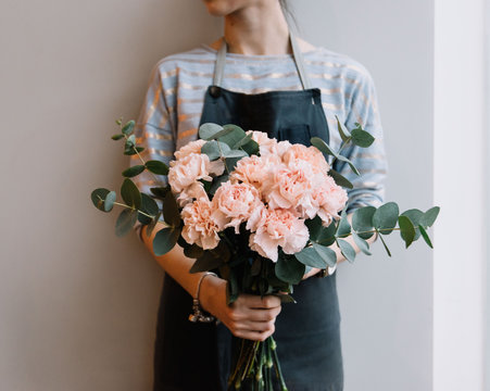 Fototapeta Young florist woman holding freshly made minimalistic blossoming flower bouquet of pastel pink carnations and eucalyptus on the grey wall background.