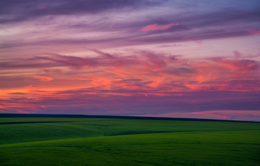 Naklejka na ściany i meble Sunset clouds over green field