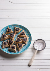 Traditional sweets for the Jewish holiday Purim. Hamantashen cookies or ears of Haman, triangular cookies with poppy seeds and raisins on a blue plate, top view, free space