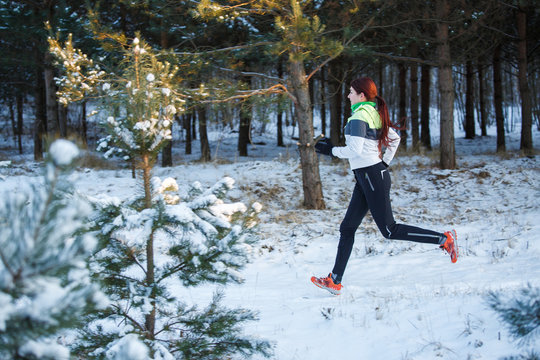 Image of young female athlete running through winter forest