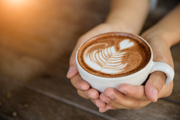 Woman hands holding cup of hot coffee latte cappuccino with heart shaped. Love, Wedding and Valentines day concept.