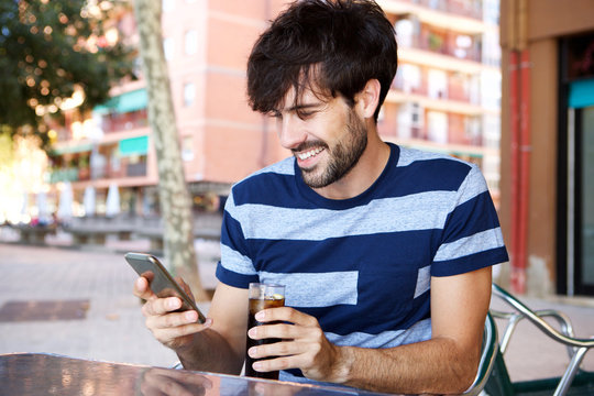 young man sitting at cafe with a drink and looking at mobile phone