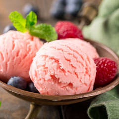 Raspberry ice cream scoops in copper bowl with forest berries and mint decoration. Summer food concept.