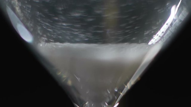 Macro view of white sand going down in hourglass on the table, measuring device