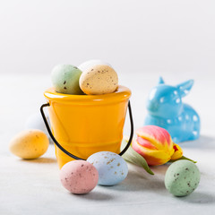 Easter composition with colored quail eggs candies in bucket and blue ceramic rabbit. Holidays concept with copy space.