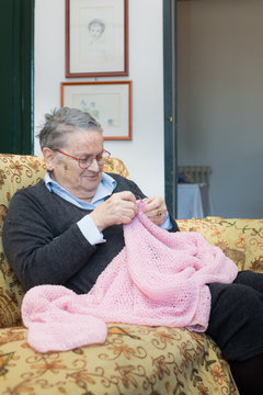 Elderly woman knitting pink wool on sofa smiling at home portrait