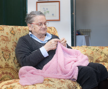 Elderly woman knitting pink wool on sofa at home portrait
