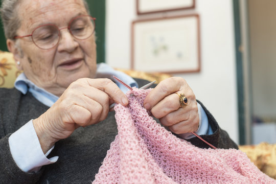 Elderly woman knitting pink wool selective focus on hands