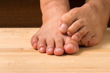 Close up a man with itchy feet uses his big toe to scratch his other foot on wooden floor.