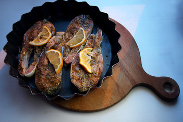 Pieces of red fish, seasoned with spices, lying in a frying pan..