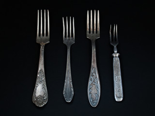 Old metal forks of different sizes lie on a black background