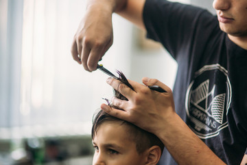 The boy getting haircut by scissor in barbershop. Barber use scissor