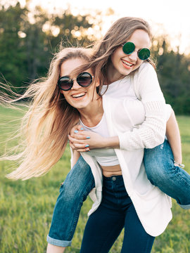 Two young women are having fun on the field. One girl is riding on another.